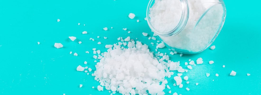 High angle view sea salt in coming out of small jar on cyan blue background. horizontal